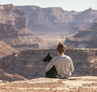 Girl hugging her dog as they sit on a cliff overlooking the Grand Canyon